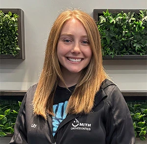 Smith Orthodontics team member Lily smiling in office with living plant wall backdrop.